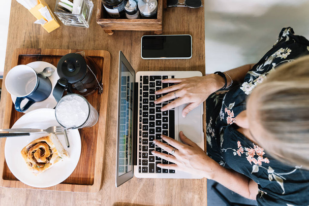 vue du dessus d'une fille travaillant sur un ordinateur portable à la cafétéria avec café et petit déjeuner autour. - Photo, image