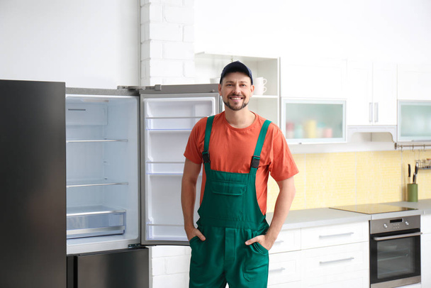 Male technician in uniform near refrigerator indoors - Фото, изображение