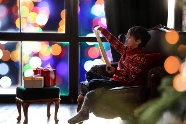 Little boy with wish list to Santa Claus near window indoors. Ch - Foto, Imagem