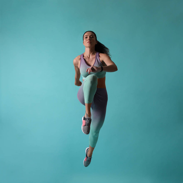 Athletic young woman running on turquoise background - Foto, Imagem