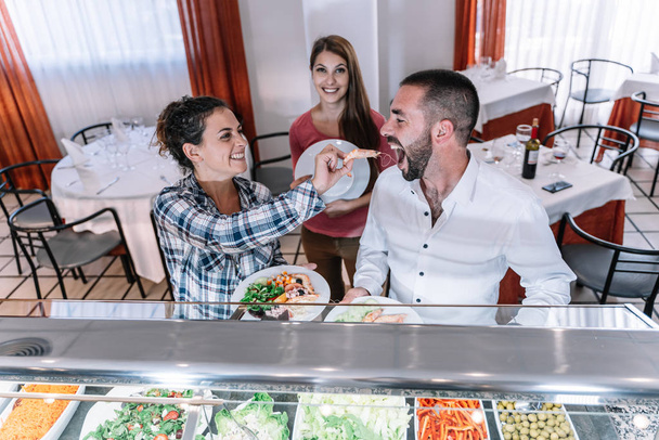 Stock photo of a girl playing feeding a shrimp to a boy in a self-service restaurant - Photo, Image