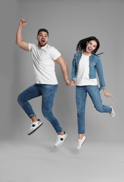 Jeune couple en jean élégant sautant sur fond gris
 - Photo, image