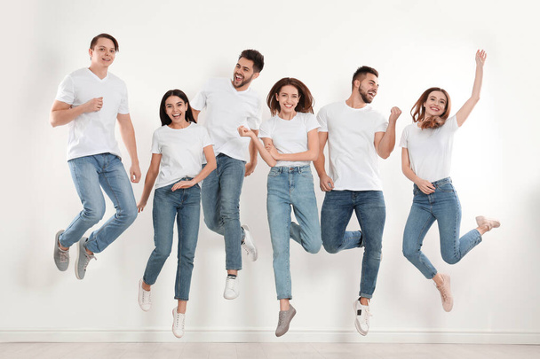 Group of young people in stylish jeans jumping near white wall - Zdjęcie, obraz