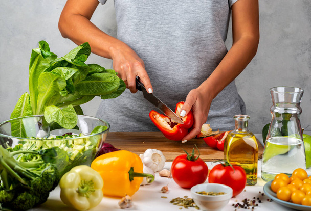 Kadın kırmızı biber keser ve mutfakta salata yapar. Sağlıklı diyet kavramı. - Fotoğraf, Görsel
