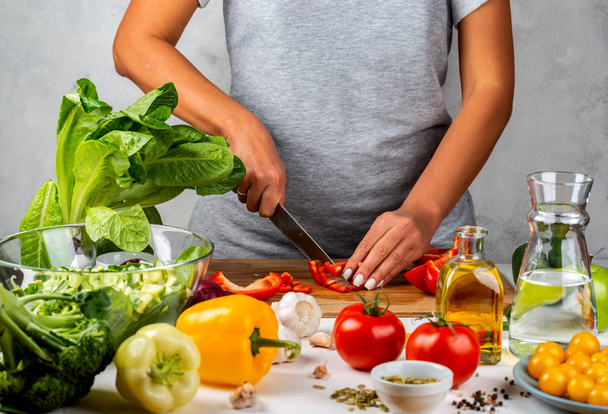 Kadın kırmızı biber keser ve mutfakta salata yapar. Sağlıklı diyet kavramı. - Fotoğraf, Görsel