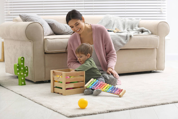 Young nanny and cute little baby playing with toys at home - Photo, image
