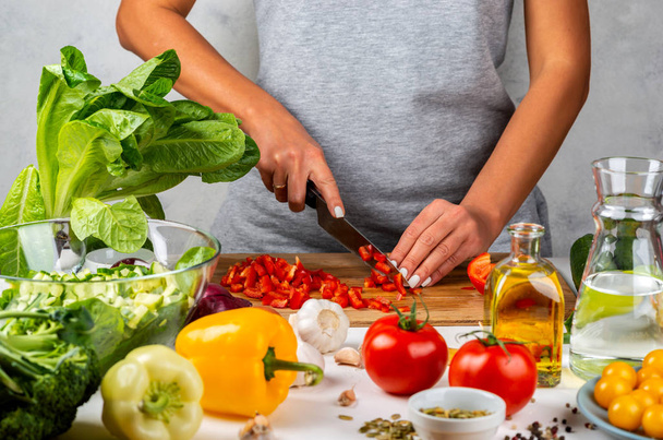 A nő pirospaprikát vág és salátát készít a konyhában. Egészséges táplálkozás koncepciója. - Fotó, kép