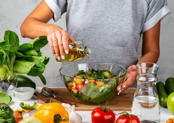 A nő olívaolajat önt egy üvegből egy salátába egy üvegtálba. Főzök a konyhában. Egészséges táplálkozás koncepciója. - Fotó, kép