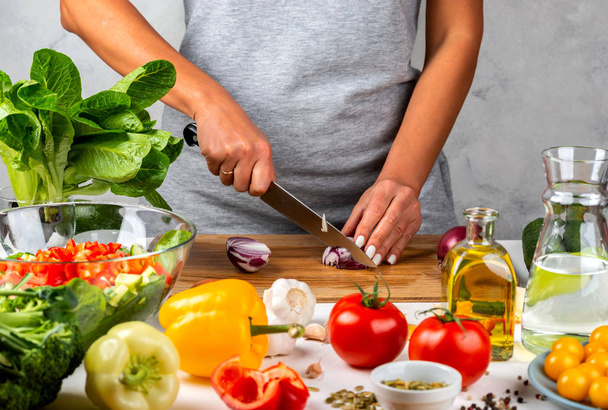 A nő hagymát vág és salátát készít a konyhában. Egészséges táplálkozás koncepciója. - Fotó, kép