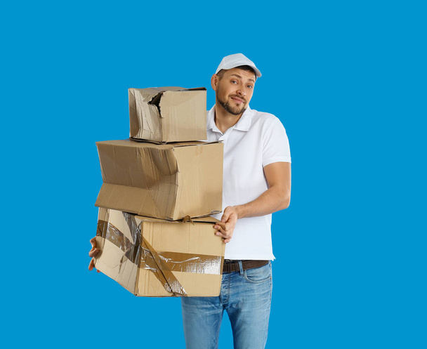 Emotional courier with damaged cardboard boxes on blue backgroun - 写真・画像