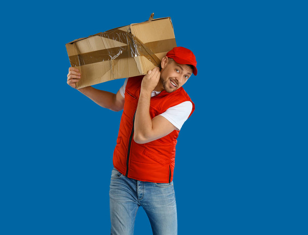 Courier with damaged cardboard box on blue background. Poor qual - Foto, afbeelding