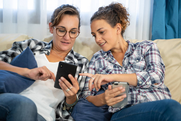 Фото двух девушек на диване с мобильниками в руке, указывающими на мобильный экран - Фото, изображение