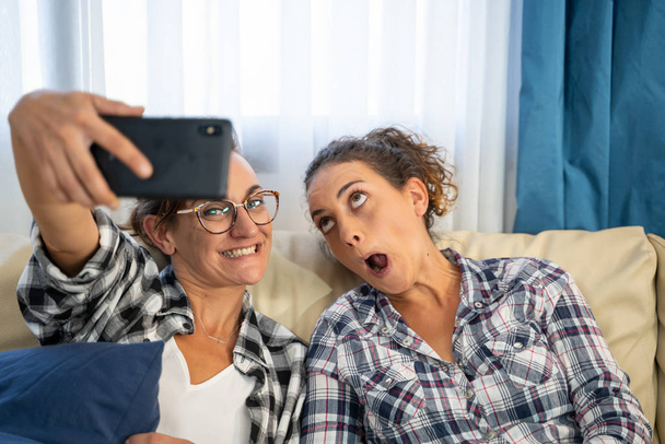 Varastossa kuva kaksi tyttöä tekee selfie hymyillen ja kasvoja istuu sohvalla - Valokuva, kuva