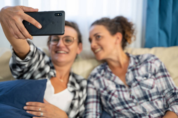 Foto en stock de una mano sosteniendo un teléfono móvil con dos chicas en el fondo haciendo una selfie - Foto, imagen