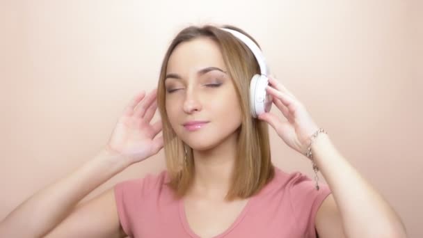 girl with pierced eyebrow and big eyes with headphones on a colored background - Imágenes, Vídeo