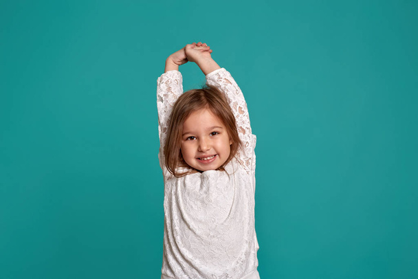 Klein meisje in een witte trui op een blauwe achtergrond. Emoties van een kind. close-up studio shot van een mooi klein meisje. - Foto, afbeelding