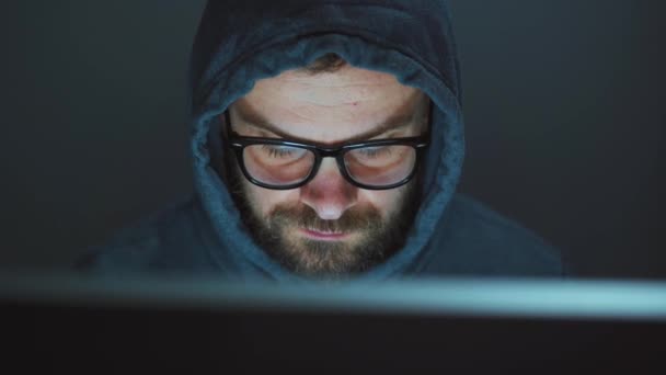 フードを着た男性ハッカーと暗いオフィスの部屋でコンピュータに取り組んでいる眼鏡。サイバー犯罪の概念 - 映像、動画