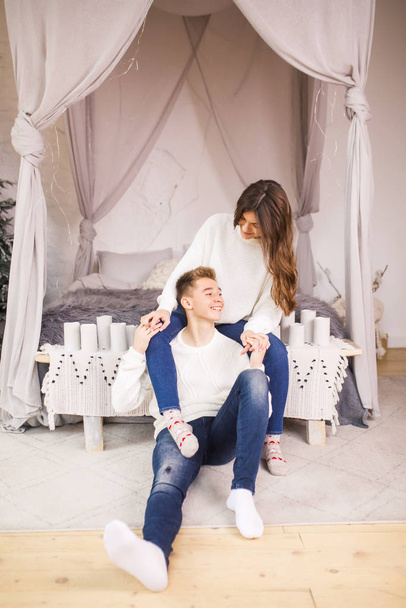 Young beautiful couple sitting on bed in a beautiful white room and smiling - Fotó, kép
