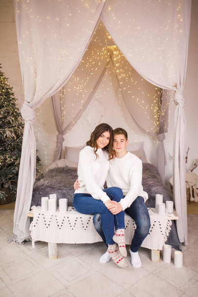 Young beautiful couple sitting on bed in a beautiful white room and smiling - Fotoğraf, Görsel