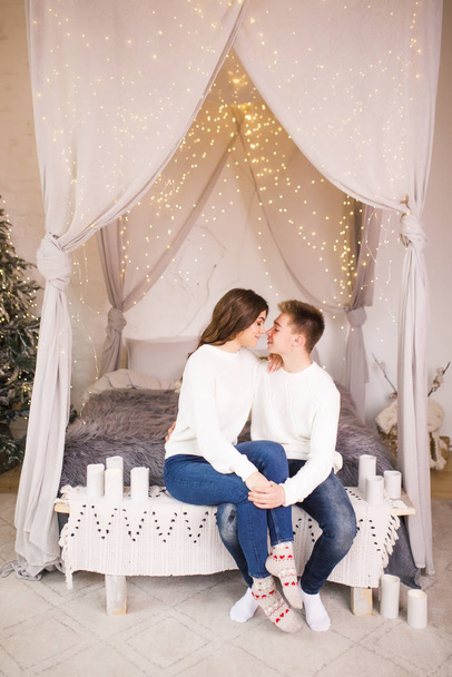Young beautiful couple sitting on bed in a beautiful white room and smiling - Фото, зображення