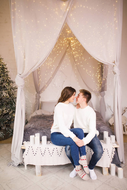Young beautiful couple sitting on bed in a beautiful white room and smiling - Foto, Bild