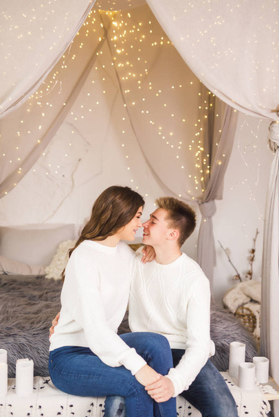 Young beautiful couple sitting on bed in a beautiful white room and smiling - Photo, image