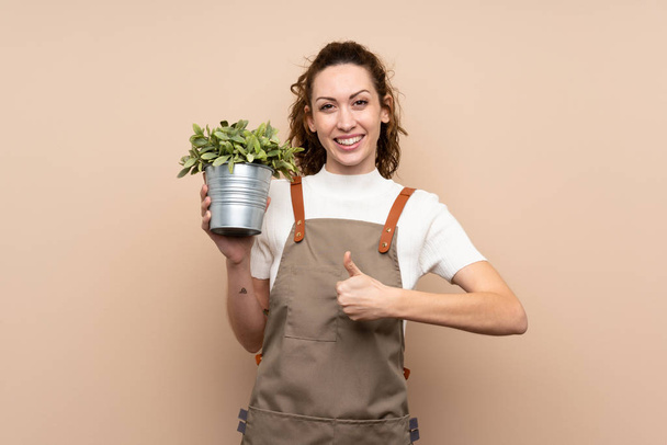 Jardinero mujer sosteniendo una planta con los pulgares hacia arriba porque algo bueno ha sucedido
 - Foto, Imagen