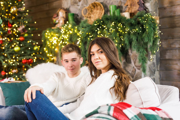 young beautiful couple sitting in a beautiful room on the bed against the background of the Christmas tree and smiling - Foto, Imagem