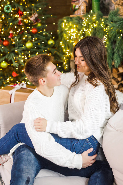 young beautiful couple sitting in a beautiful room on the bed against the background of the Christmas tree and smiling - Photo, image