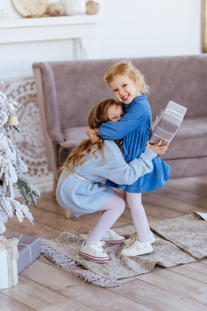 Two cute adorable little sisters near christmas tree in cozy living room. - Фото, зображення