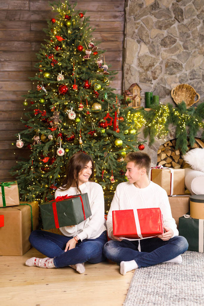 Young beautiful couple sits on a background of the Christmas tree in their hands holding gifts and smiling - Foto, immagini