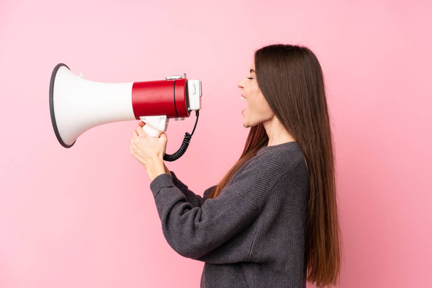 Young woman over isolated pink background shouting through a megaphone - Foto, Bild
