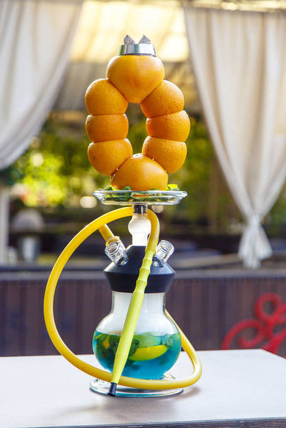 Hookah on oranges. Citrus hookah. Hookah with round clear bulb with a red liquor. A bowl of hookah made of oranges. Lots of smoke. - Фото, зображення
