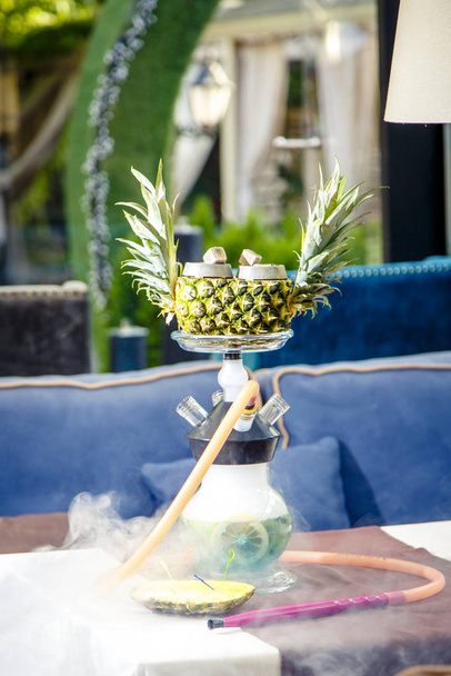 Hookah on pineapple. Pineapple hookah. Hookah with round clear bulb in which the red liqueur float aplysina and chopped mint leaves. The bowl of the hookah pineapple.  - 写真・画像