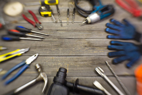 Μοντέρνα εργαλεία σε ξύλινο τραπέζι. Στο τραπέζι είναι: Puncher, σφυρί, πένσα, χαρτικά μαχαίρι, κατσαβίδια, ψαλίδια, τρυπάνια σε σκυρόδεμα, ηλεκτρικό κατσαβίδι, γάντια κατασκευής, σμίλες. - Φωτογραφία, εικόνα