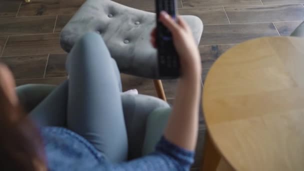 Mulher está sentada em uma cadeira, assistindo TV com tela verde, trocando de canal com controle remoto. Chave Chroma. Interior
 - Filmagem, Vídeo