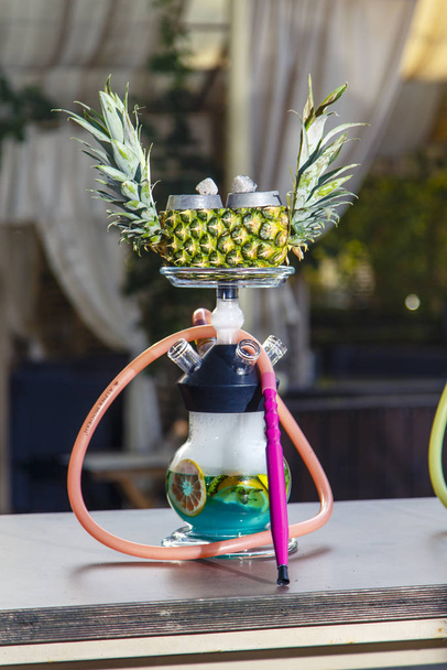 Hookah on pineapple. Pineapple hookah. Hookah with round clear bulb in which the red liqueur float aplysina and chopped mint leaves. The bowl of the hookah pineapple. - 写真・画像