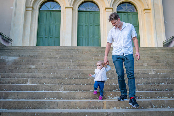 πατέρας και κόρη κατεβαίνουν τις σκάλες και κρατιούνται χέρι χέρι. - Φωτογραφία, εικόνα