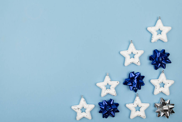 Holiday decorations. Creative composition made of white stars - Christmas tree toys, classic blue and silver bows on light blue background. top view, closeup. Copy space - Фото, изображение