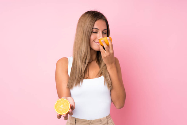 junge blonde Frau über isoliertem Hintergrund mit einer Orange - Foto, Bild