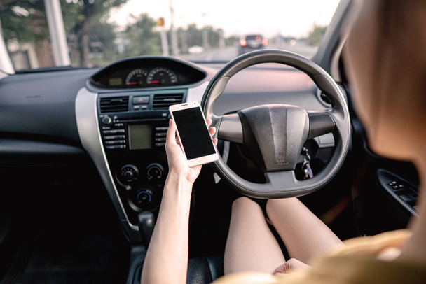 Young woman in car checking her smartphone while driving - 写真・画像