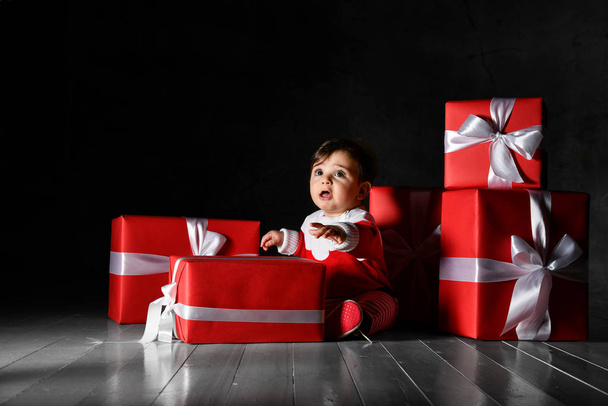 Little baby babe with santa costume with red boxes on a dark background - Fotó, kép