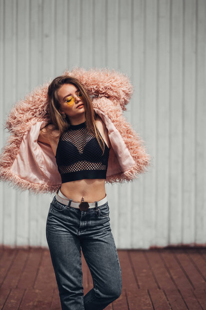 Portrait of One Stylish Girl in Pink Coat and Modern Yellow Sunglasses Posing on Street - Photo, Image