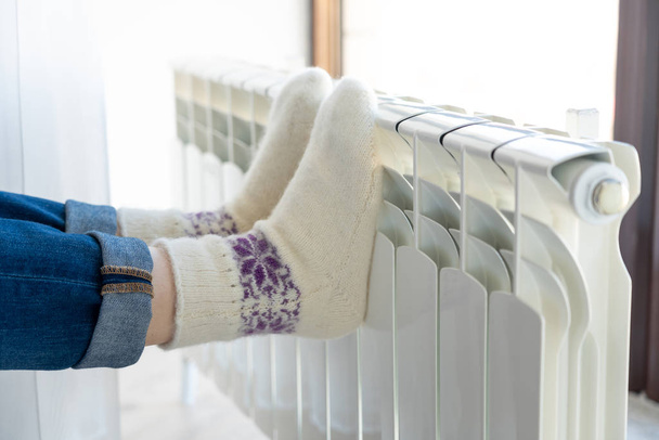 Donna che si scalda con i piedi sul riscaldatore indossando calzini di lana
 - Foto, immagini