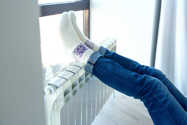 Woman warming up with feet on heater wearing woolen socks, blue toning - 写真・画像