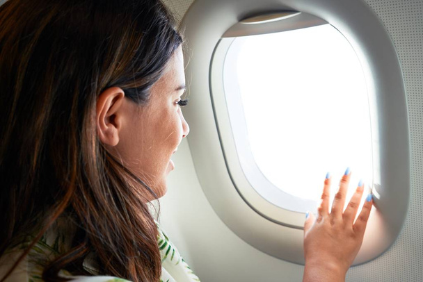 Молодая женщина путешественник сидит внутри самолета в аэропорту с видом на небо из окна
 - Фото, изображение