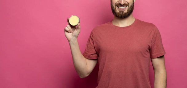 Close-up image of handsome bearded man holding beard balm on pink background. - Foto, imagen