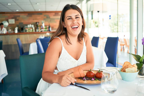 Young beautiful woman sitting at restaurant enjoying summer vacation eating delicious food - Foto, Imagen