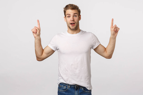 You certainly need download it. Amuased attractive and excited, astounded blond cute bearded man in white t-shirt, pointing fingers up, gasping astonished, speechless, see something interesting - Photo, Image