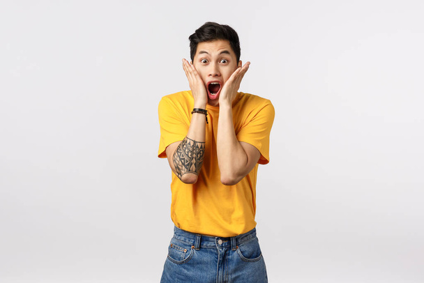 Impressed, shocked young asian man hear outstanding news, holding hands on cheeks, drop jaw scream from amazement and excited, see something stunning and cool, standing white background - Foto, immagini
